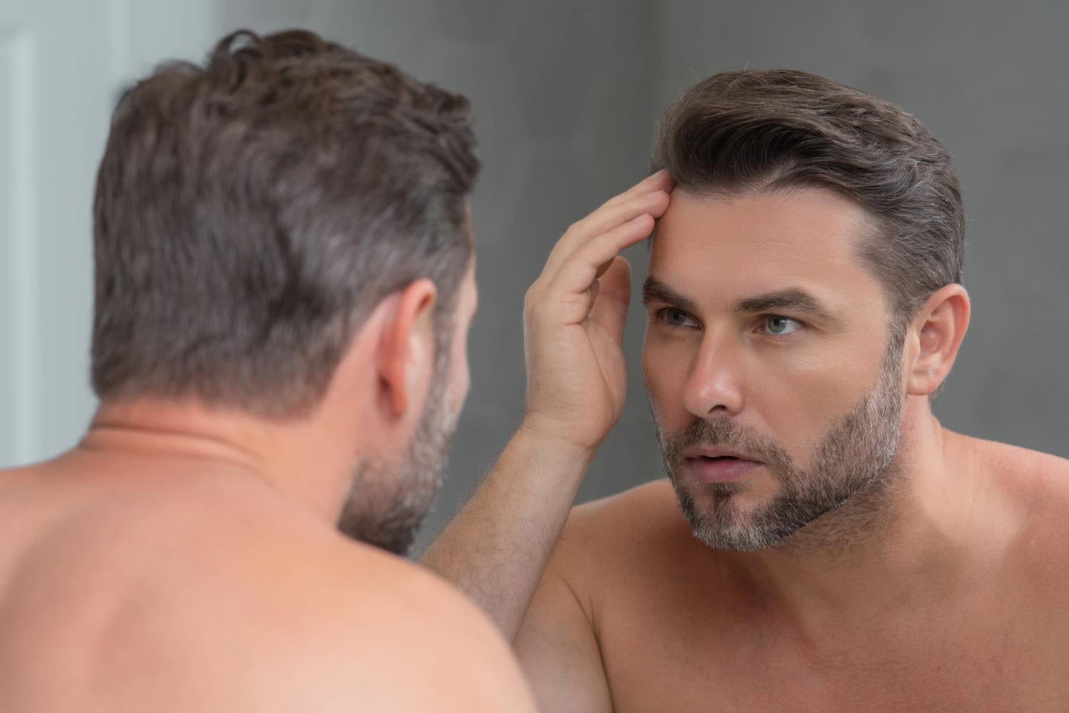 Ein Mann, der nach der Haartransplantation in den Spiegel schaut und seine Haare betrachtet