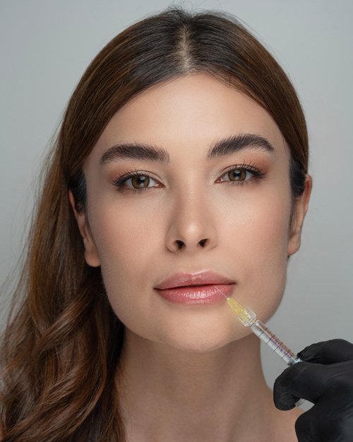 Schöne Frau mit einer Nadel am Mund bei der Lippenunterspritzung